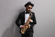 Man playing a sax and leaning against gray wall