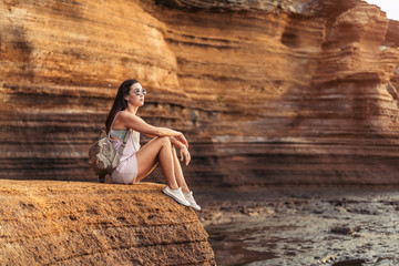 Wall Mural - Pretty long hair brunette tourist girl relaxing on the stones near sea.