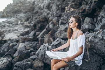 Wall Mural - Pretty long hair tourist girl relaxing on the stones near sea.