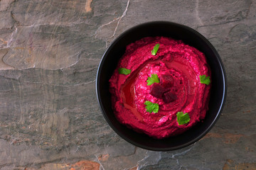 Wall Mural - Beet hummus dip in a black bowl, above view on a dark background