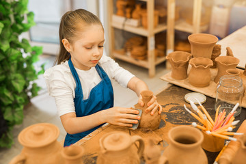 Sticker - beautiful little girl making a pot of clay in a pottery workshop