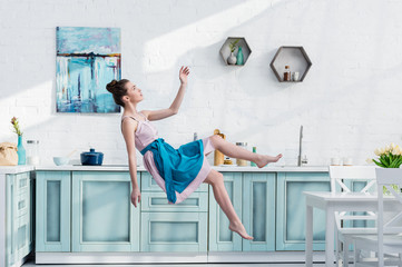 Wall Mural - young elegant woman in apron and dress flying in air in kitchen