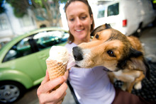 A Woman With Her Dog That Is Licking Her Ice Cream Cone.