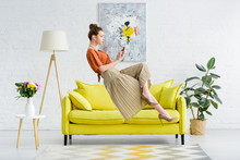 Elegant Young Woman Levitating In Air And Using Digital Tablet In Living Room