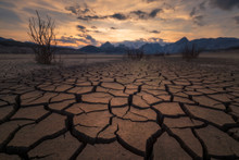 Earth Cracked By Extreme Drought Below A Dramatic Sunset.
