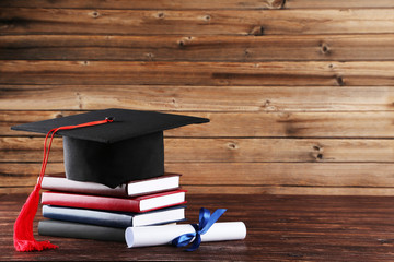 Graduation cap with diploma and stack of books on brown wooden table