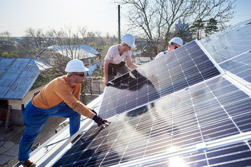 Male workers installing solar photovoltaic panel system. Electricians mounting blue solar module on roof of modern house. Alternative energy ecological concept.