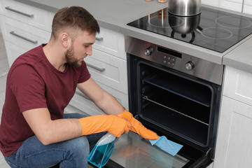 Wall Mural - Young man cleaning oven with rag and detergent in kitchen