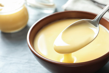 Spoon of pouring condensed milk over bowl on table, closeup with space for text. Dairy products