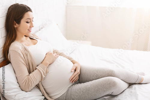 Fotografía Happy pregnant lady caressing her belly, lying in bed