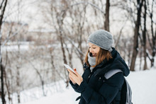 Happy Young Woman In Hat With Phone Texting Outdoors In Winter Park
