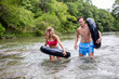 © Cavan Images - Young couple walking down river with tubes