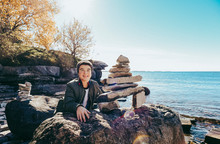 Teenage Boy Smiling Next To Rock Sculpture (inukshuk) By The Lake.