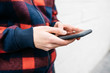 © Westend61 - Hands of young man with checkered jacket using phone