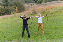 Two Archer Standing On A Meadow Aiming With Her Bows