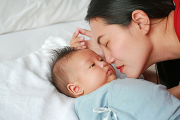 Close up mother kissing newborn baby boy lying on the bed.