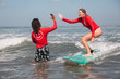 © Hagen Production - Surf instructor coach guide and student on surfboard giving high five at surf school lesson, learning surfing at Seminyak beach, Bali, Indonesia