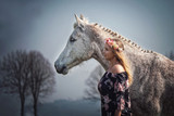 Fototapeta Konie - Portrait Frau und weißes Pferd Schimmel in Blumenkleid mit Blumenkranz im Haar im Wald in der Natur mit Himmel im Hintergrund