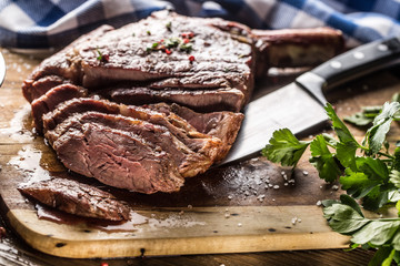 Freshly grilled tomahawk steak on slate plate with salt pepper rosemary and parsley herbs. Sliced pieces of juicy beef steak