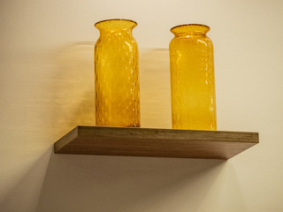 Two yellow glass vases stand on a wall shelf