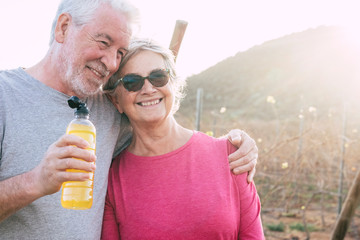 Happy cheerful aged senior couple smile and enjoy together forever life in outdoor country side with sun in backlight after a healthy fitness session