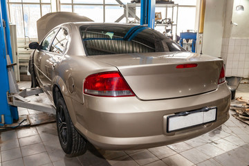 Beige used car with an open hood raised on a lift for repairing the chassis and engine in a vehicle repair shop. Auto service industry.