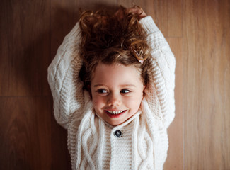 A portrait of small girl with white knitted sweater lying on the floor, a top view.