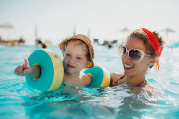 Wall Mural - A small toddler boy with armbands and mother swimming in water on summer holiday.