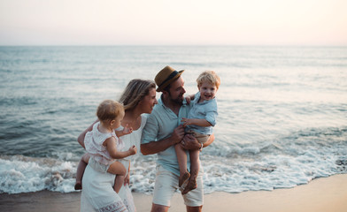 A young family with two toddler children standing on beach on summer holiday.