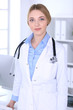 © rogerphoto - Young woman doctor at work in hospital looking at camera. Blue colored blouse of therapist looks good. Medicine and healthcare concept