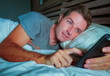 © TheVisualsYouNeed - young attractive man smiling happy lying on bed at night using social media app on mobile phone texting or having video call in communication lifestyle