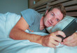 © TheVisualsYouNeed - young attractive man smiling happy lying on bed at night using social media app on mobile phone texting or having video call in communication lifestyle