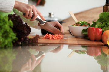 Unknown human hands cooking in kitchen. Woman slicing red tomatoes. Healthy meal, and vegetarian food concept