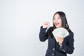 Wall Mural - A young businesswoman holds a dollar note on a white brick wall background.