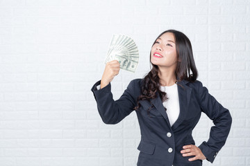 Wall Mural - A young businesswoman holds a dollar note on a white brick wall background.