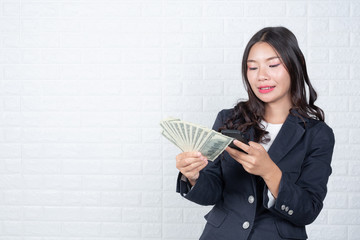 A young businesswoman holds a dollar note on a white brick wall background.