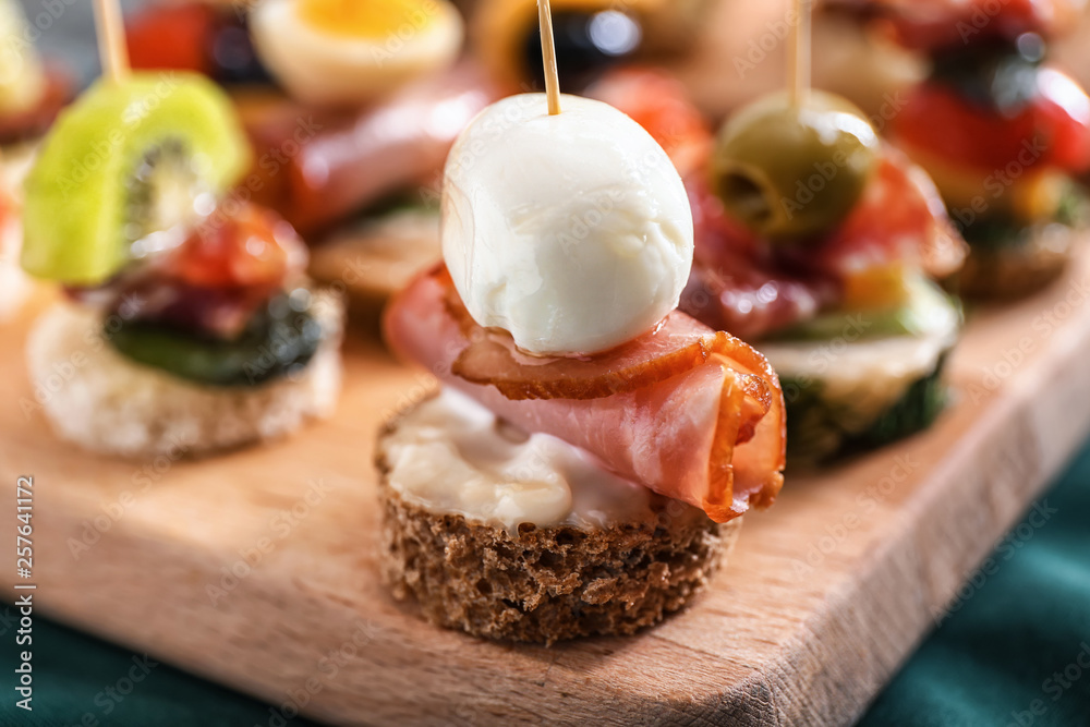 Tasty canapes on wooden board, closeup