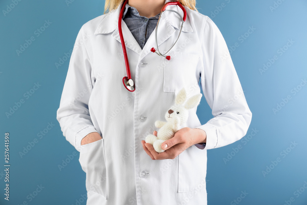 Female pediatrician with bunny toy on color background