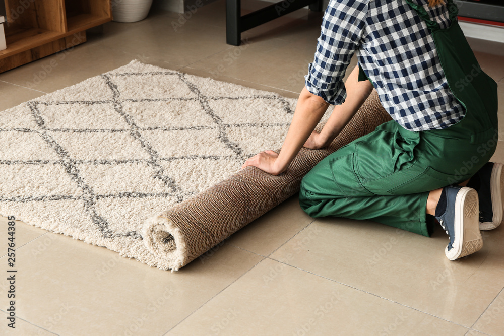 Worker rolling carpet on floor in room
