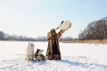 Northern Shaman Beats Tambourine Performing A Rite Calls Spring. Husky Dogs. Winter Landscape