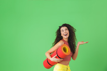 Wall Mural - Photo of athletic woman 20s smiling and carrying yoga mat during workout