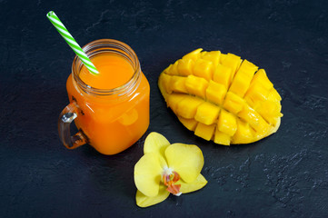 Wall Mural - Mango smoothie in a glass jar and fresh mango on a black background. Mango shake. Tropical fruit concept.