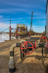 Oil field in Siberia. In a row are oil producing wells. In the background, work is underway to overhaul the well. In the foreground is a manifold with valves.