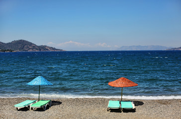 Sun beds on a beach with colorful sun umbrellas with deep blue sea on the background and an island on the horizon. Family vacations place. 