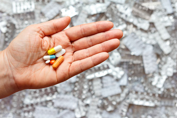 Hand with many different tablets in front of empty pill sheets, comorbidity concept