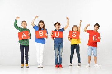  Abuse makes you monster. Group of screaming angry serious children with red banners isolated on white studio background. Education and advertising concept. Protest and children's rights concepts.