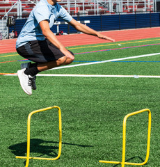 Young male athlete jumping over two foot hurdle