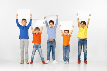 Wall Mural - Group of angry children with a white empty banners isolated in studio background. Education and advertising concept. Protest and children's rights concepts.