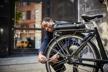 Smiling Man Locking Electric Bicycle On Sidewalk