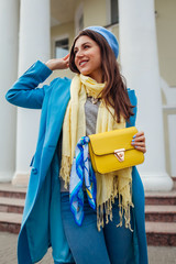 Wall Mural - Young woman in trendy blue coat walking in city holding stylish handbag. Spring female clothes and accessories. Fashion